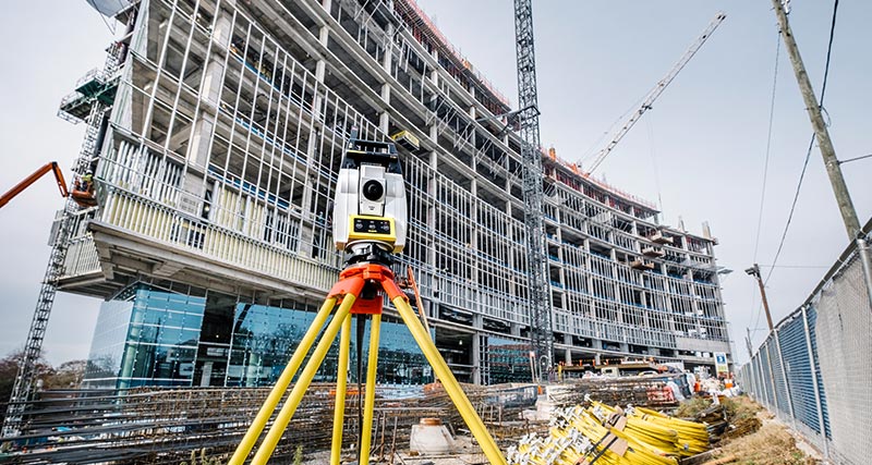 Die automatisierte Bautotalstation Leica iCON iCR70 vor einem neuen Gebäude mit einem Bauarbeiter in gelber Weste.