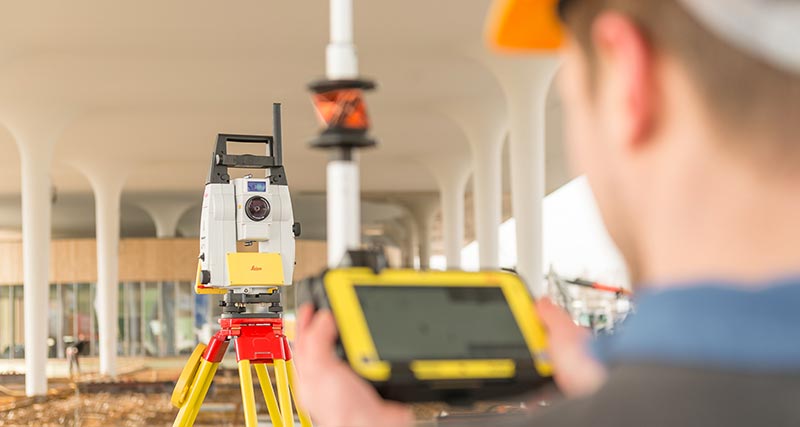 Leica iCON iCR80 no canteiro de obras com um operário em frente dele, segurando um bastão para prisma com uma controladora de campo CC80.