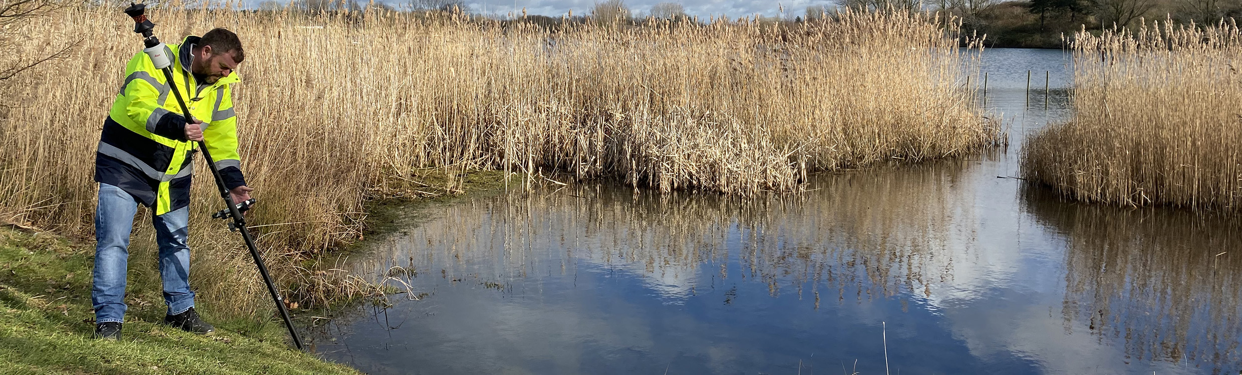 Surveyor safely measures points to map a lake border with a tilted Leica AP20 prism pole.